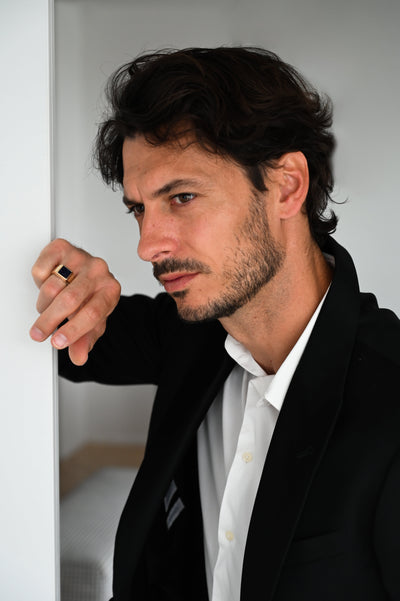 A man in a suit leaning against a wall, showcasing the Goldstone Signet Ring.