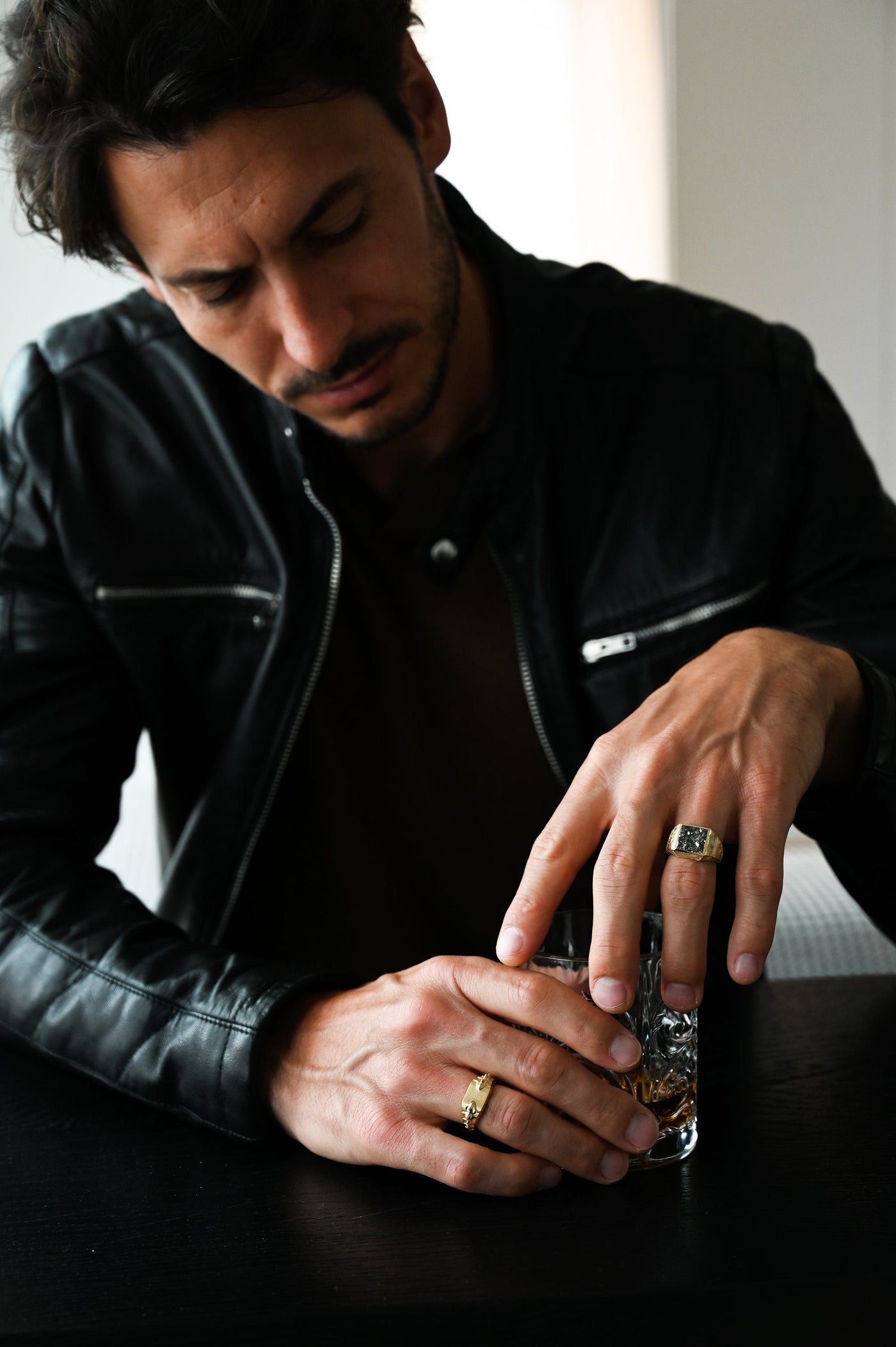 A man in a black leather jacket holds a glass of whiskey, showcasing the Pyrite Signet Ring.