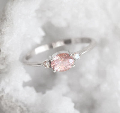 Oval-shaped pink peach sapphire ring with white side diamonds