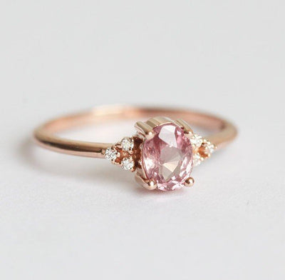 Oval-shaped peach pink sapphire ring with white side diamonds