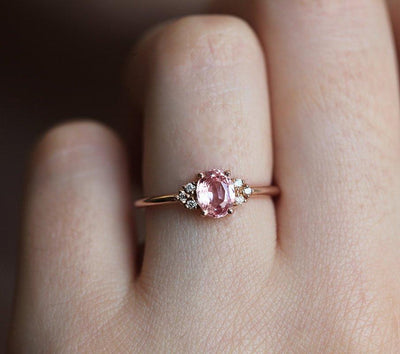 Oval-shaped peach pink sapphire ring with white side diamonds