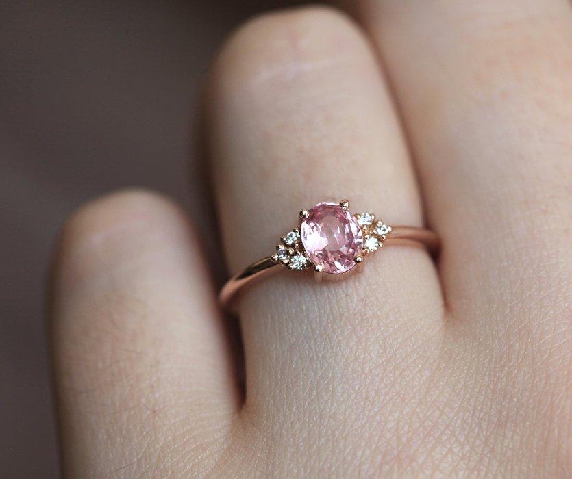 Oval-shaped peach pink sapphire ring with white side diamonds