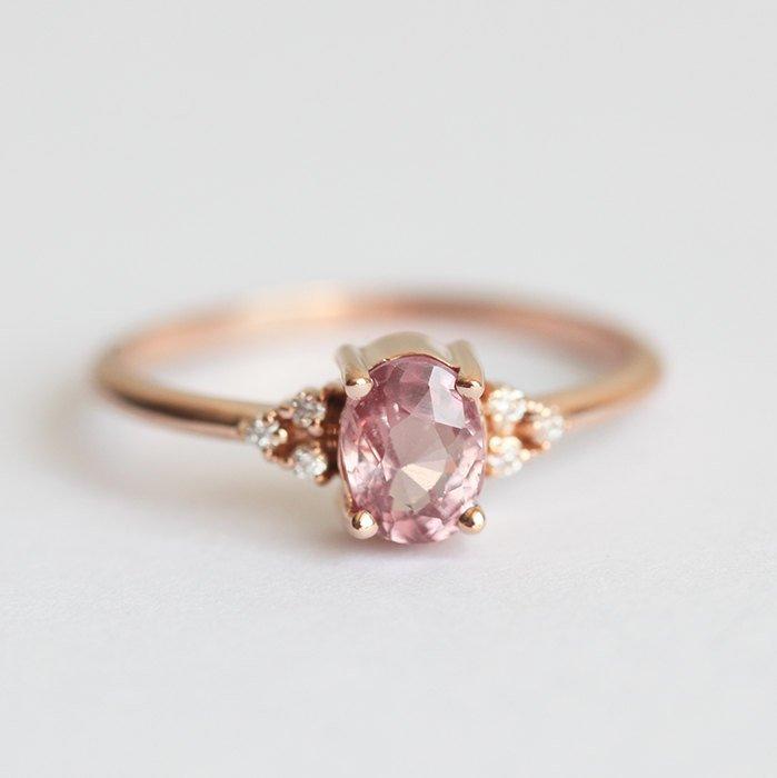 Oval-shaped peach pink sapphire ring with white side diamonds