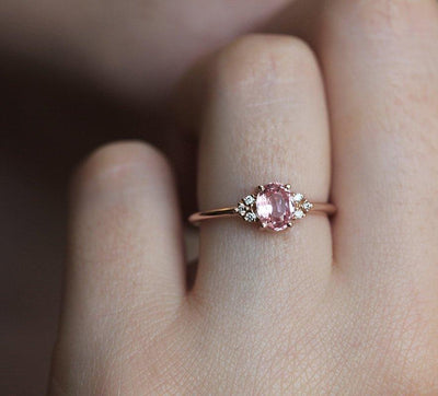 Oval-shaped peach pink sapphire ring with white side diamonds