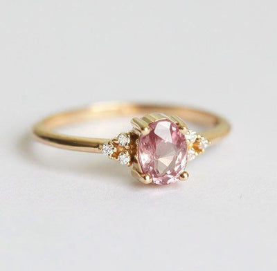 Oval-shaped peach pink sapphire ring with white side diamonds