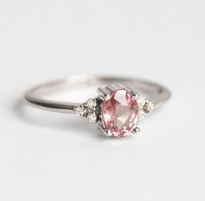 Oval-shaped peach pink sapphire ring with white side diamonds