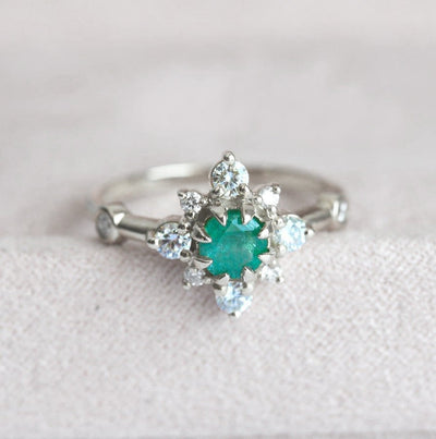 Emerald ring with diamond halo, featuring a round green emerald stone and sparkling diamonds. Vintage-inspired yet modern.