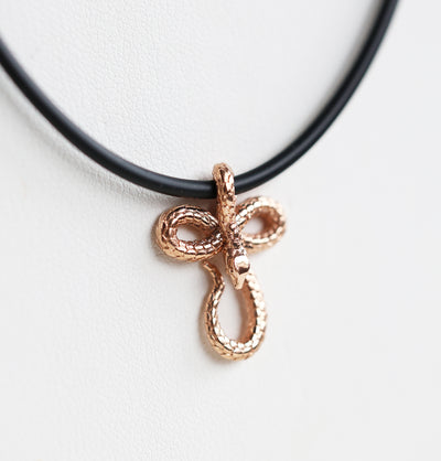 A 14K gold snake pendant necklace, featuring an intricate design on a sleek natural rubber cord—bold, symbolic, and effortlessly stylish.