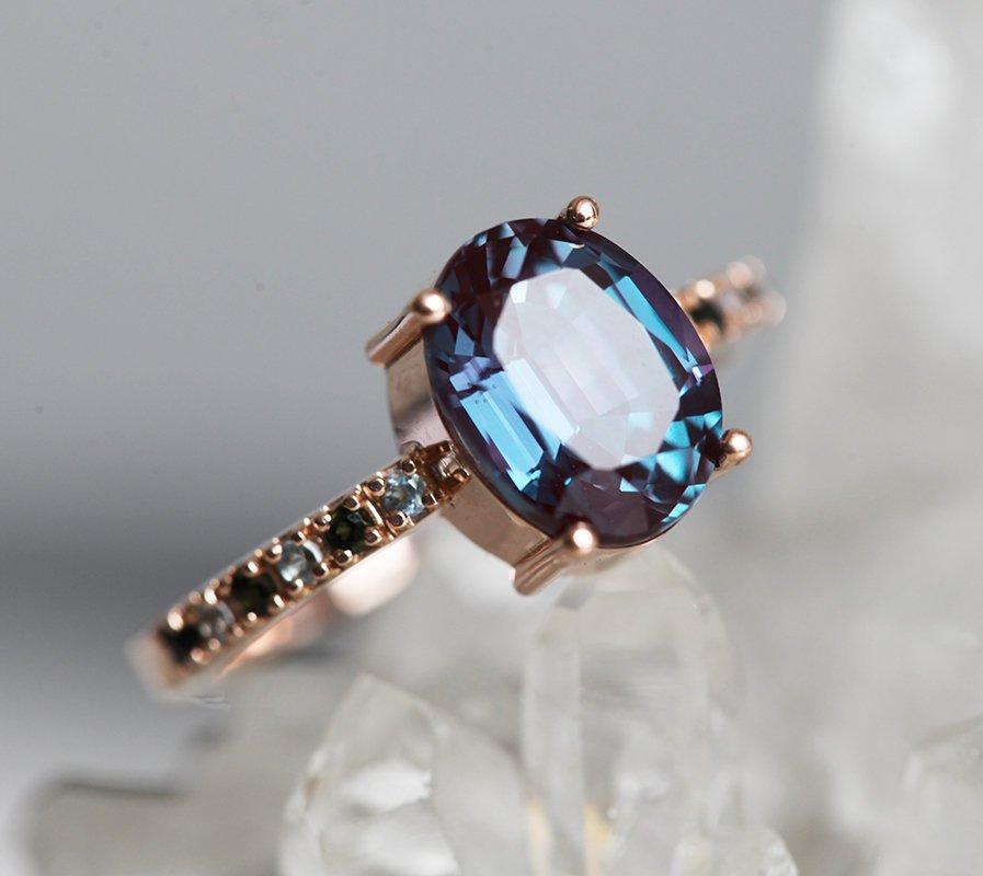 Teal Oval Alexandrite Ring with Side Blue Topaz Stones and Black Round Diamonds Nested in the Band