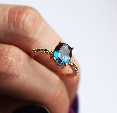 Teal Oval Alexandrite Ring with Side Blue Topaz Stones and Black Round Diamonds Nested in the Band