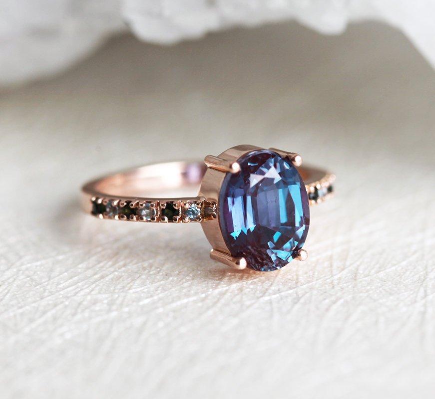Teal Oval Alexandrite Ring with Side Blue Topaz Stones and Black Round Diamonds Nested in the Band