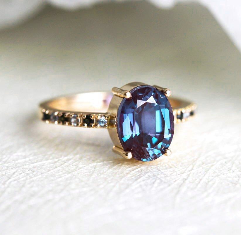 Teal Oval Alexandrite Ring with Side Blue Topaz Stones and Black Round Diamonds Nested in the Band