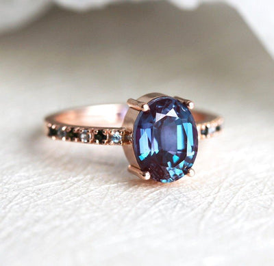 Teal Oval Alexandrite Ring with Side Blue Topaz Stones and Black Round Diamonds Nested in the Band