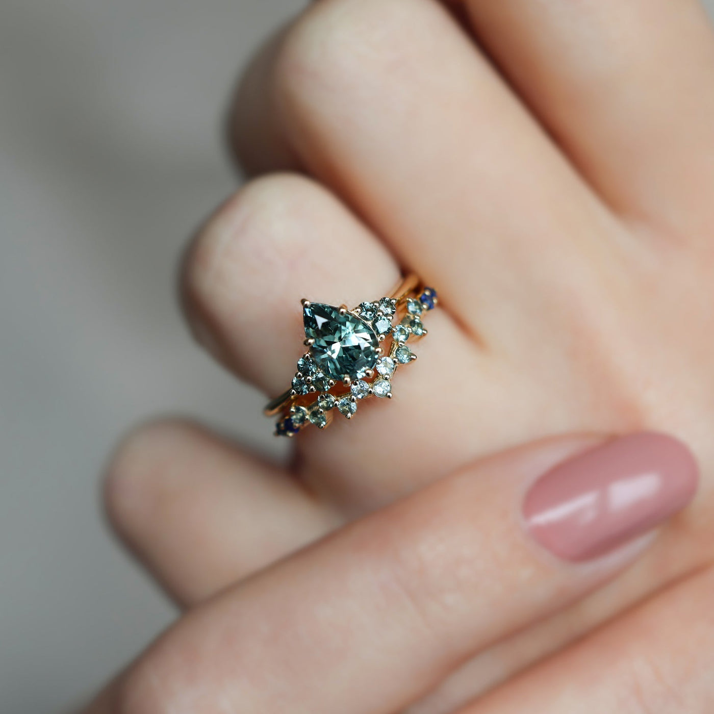Pear-shaped teal sapphire cluster ring with curved sapphire band and diamonds