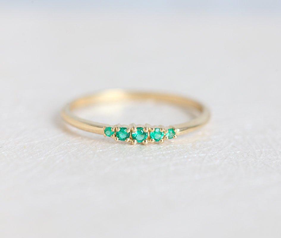 A delicate gold ring with a row of small, sparkling green gemstones.
