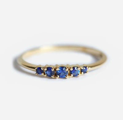Close-up of a gold ring featuring five round-cut sapphires with deep blue hues, set in a prong setting.