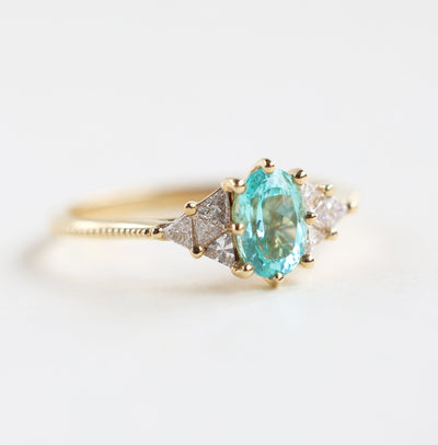 Close-up of a Paraiba Tourmaline engagement ring with triangle diamonds on sides. Crafted in 14k gold.