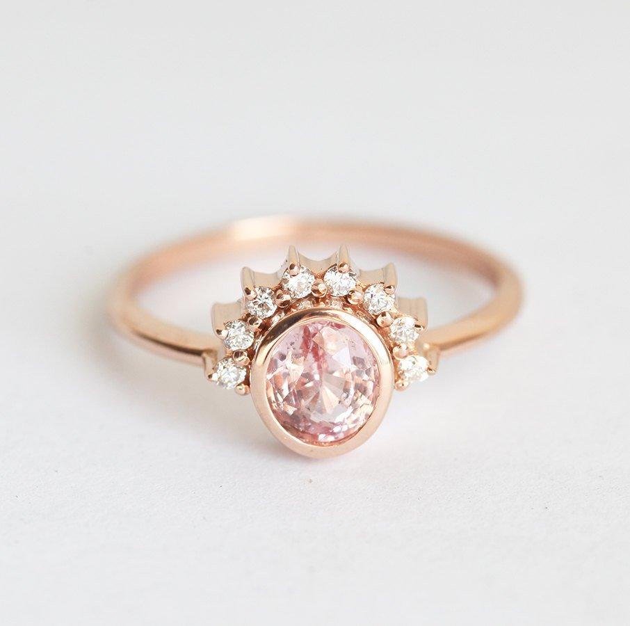 Oval-shaped peach pink sapphire ring with diamond halo