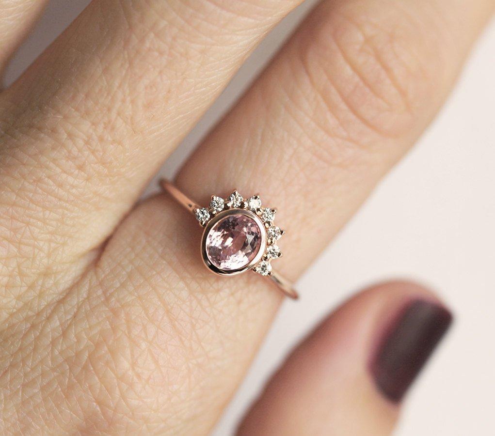 Oval-shaped peach pink sapphire ring with diamond halo