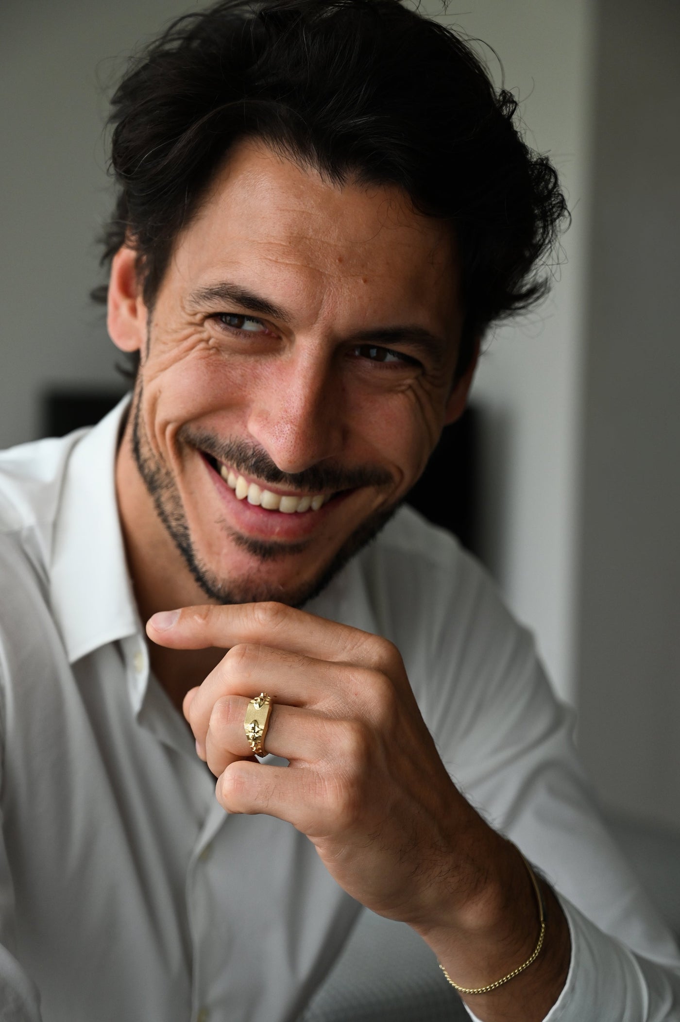 A smiling man wearing a Snake Spine Signet Ring in gold.