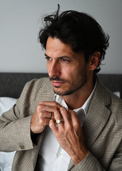 A man in a suit buttoning his shirt, showcasing the Snake Spine Signet Ring in gold.