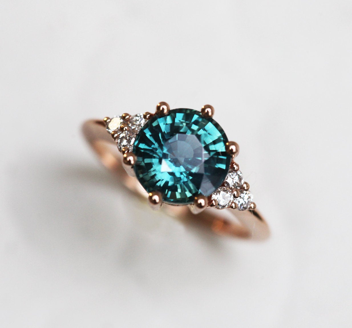 Round teal sapphire ring with white side diamonds