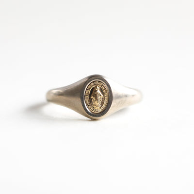 Minimalist Virgin Mary signet ring in 14k or 18k gold, featuring a coin-like center. Dimensions: 7x5mm. Customizable with gemstones.