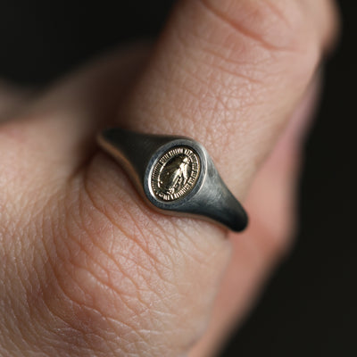 Close-up of a minimalist Virgin Mary signet ring in 14K or 18K gold.