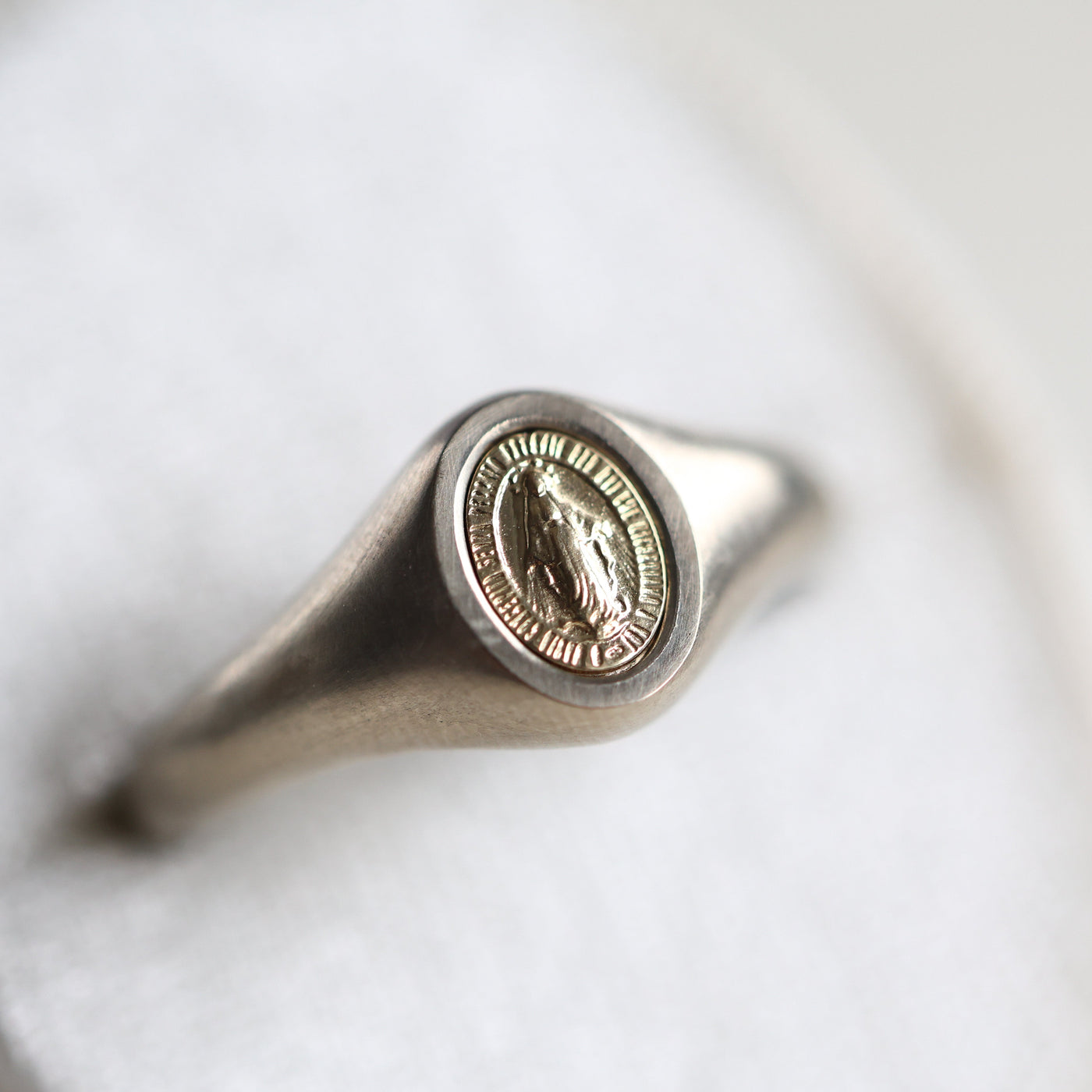 Close-up of a platinum Virgin Mary signet ring, minimalist design, 14K or 18K gold options available, Mary measures 7x5mm.