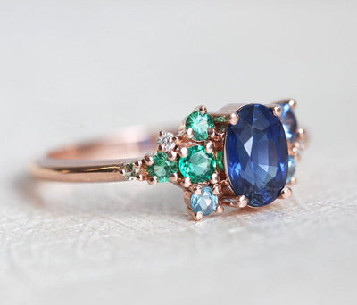 Oval-shaped royal blue sapphire cluster ring with topaz, emerald, sapphire and diamond gemstones