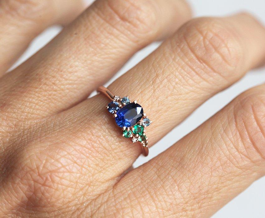 Oval-shaped royal blue sapphire cluster ring with topaz, emerald, sapphire and diamond gemstones