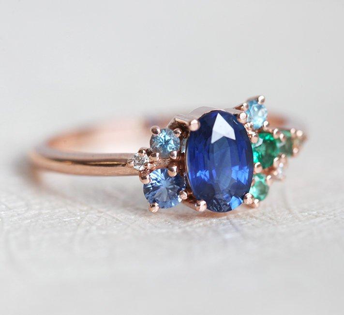 Oval-shaped royal blue sapphire cluster ring with topaz, emerald, sapphire and diamond gemstones