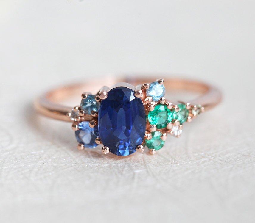 Oval-shaped royal blue sapphire cluster ring with topaz, emerald, sapphire and diamond gemstones