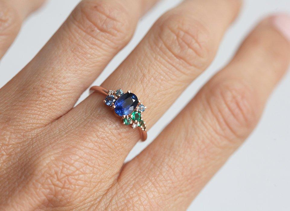 Oval-shaped royal blue sapphire cluster ring with topaz, emerald, sapphire and diamond gemstones