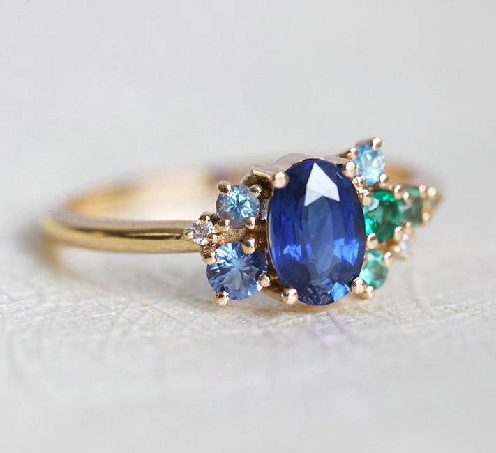 Oval-shaped royal blue sapphire cluster ring with topaz, emerald, sapphire and diamond gemstones