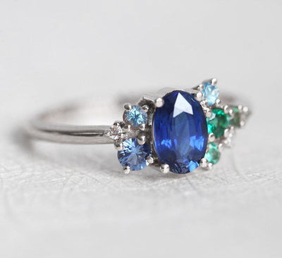 Oval-shaped royal blue sapphire cluster ring with topaz, emerald, sapphire and diamond gemstones