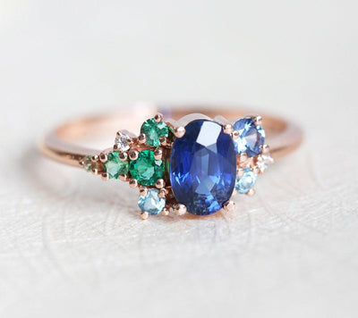 Oval-shaped royal blue sapphire cluster ring with topaz, emerald, sapphire and diamond gemstones